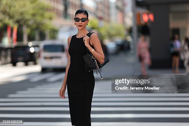 Fashion guest is seen wearing a sleek, minimalist style. Her attire consists of a black, sleeveless, knee-length dress. Her accessories include a...