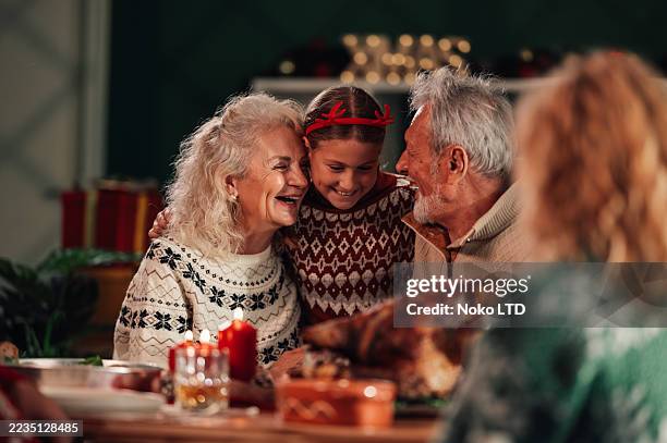 grandparents embracing granddaughter at christmas dinner table - cosy christmas stock pictures, royalty-free photos & images