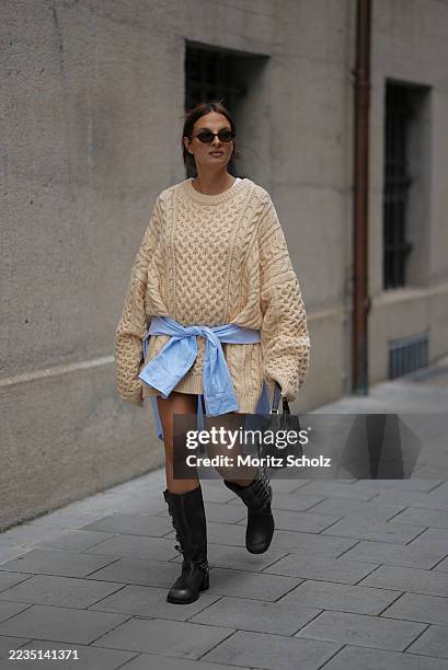 Anna Winter is seen wearing an oversized beige cable knit sweater with a chunky texture and long, relaxed sleeves from The Frankie Shop; a light blue...