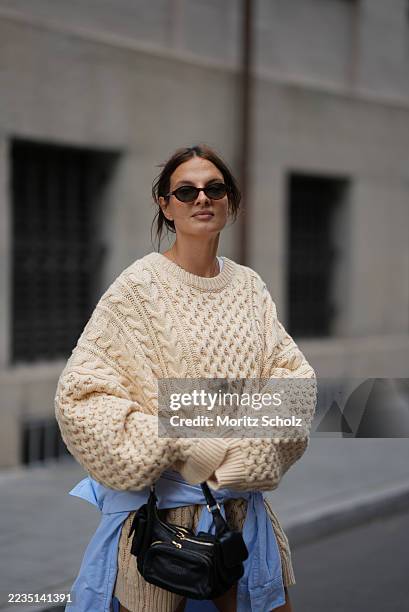 Anna Winter is seen wearing an oversized beige cable knit sweater with a chunky texture and long, relaxed sleeves from The Frankie Shop; a light blue...