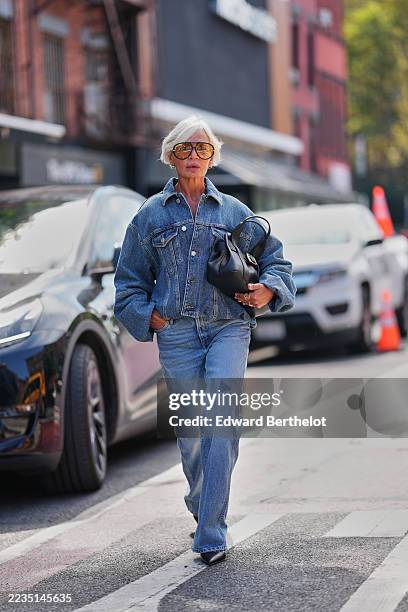 Grece Ghanem wears a short silvery-white cropped bob with a side-swept fringe, oversized aviator sunglasses with amber-tinted lenses and black frames...