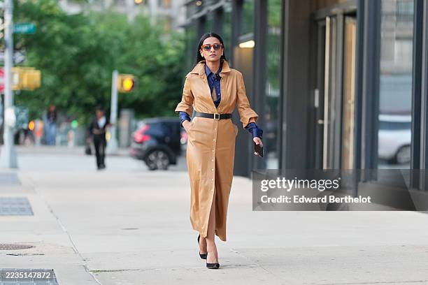Guest wears long straight dark hair parted in the center, tortoiseshell rectangular sunglasses with brown lenses, a tan leather long belted...
