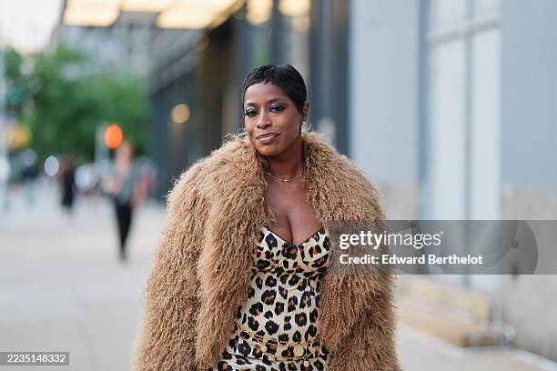 Guest wears a short cropped black pixie haircut, small gold stud earrings and a thin gold chain necklace, a camel-colored shaggy fur coat draped over...