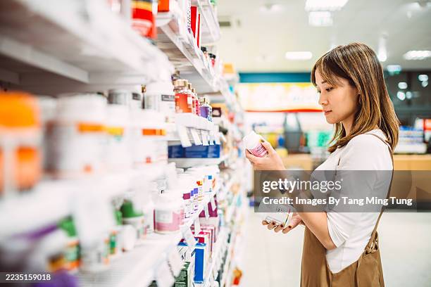 woman shopping for vitamins and supplements in store aisle - pharmacy aisle stock pictures, royalty-free photos & images