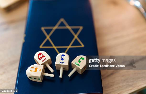 four dreidels resting on a hanukkah book with star of david - torah stock pictures, royalty-free photos & images