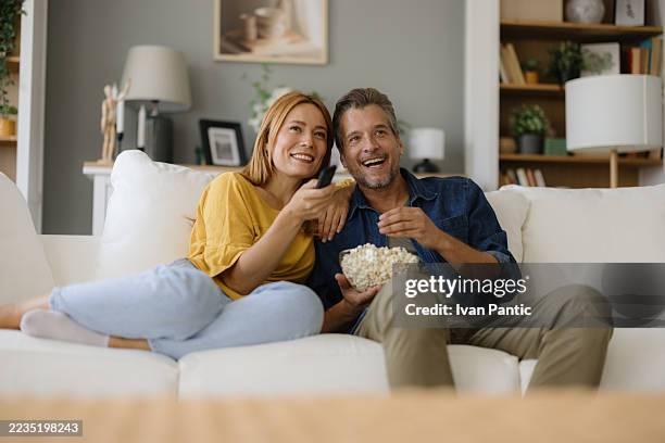 couple relaxing on sofa, watching television and eating popcorn - white dress stock pictures, royalty-free photos & images
