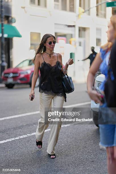 Guest wears long straight brown hair parted in the middle, round wire-frame sunglasses with dark lenses, a thin black knotted cord choker with a...