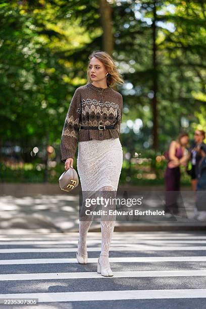 Guest wears chin-length wavy blonde hair with a side part, carries a small crescent-shaped top-handle leather bag from Fendi in taupe with gold...