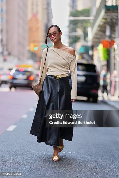 Guest wears hair pulled back into a low bun with a long face framing strand at the front, oval tortoiseshell sunglasses with brown lenses, round gold...