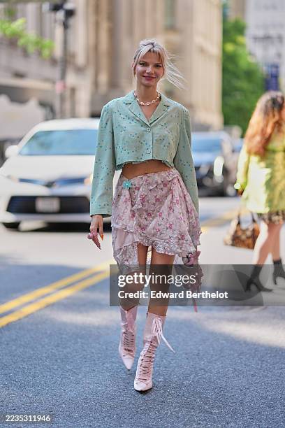 Guest wears a blonde topknot with loose tendrils, a white pearl necklace, a small pale-pink leather top-handle bag with hanging ribbon fringe, a...