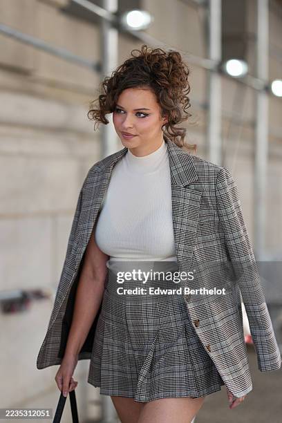 Isabella Briggs wears a curly updo with loose tendrils framing the face, a gold-tone wristwatch, a small rectangular black croc-embossed leather...