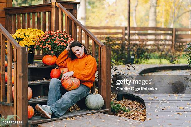 woman relaxing on porch steps with pumpkins and flowers in autumn - monat stock-fotos und bilder
