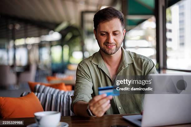 man shopping online using laptop computer and credit card at a cafe - man reading card stock pictures, royalty-free photos & images
