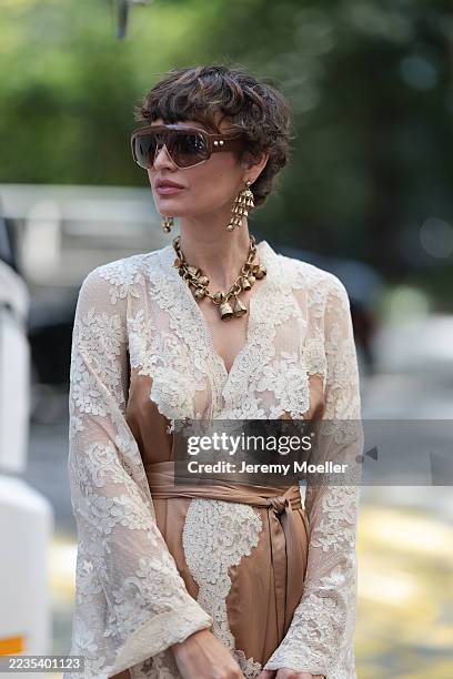 Irina Kro Eicke is seen wearing a long, two-piece ensemble of a top and wide-legged pants. The outfit's color palette is dominated by a warm, earthy...
