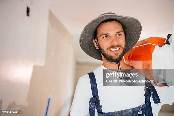 operaio che trasporta un sacco in un cantiere edile - sacchi cemento foto e immagini stock