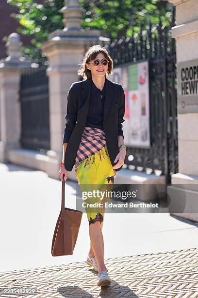 Guest wears a short brown bob with side-swept bangs, round tortoiseshell sunglasses, a silver wristwatch and an orange bracelet, a brown leather tote...