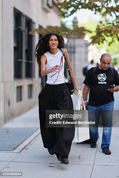 Guest wears long voluminous dark curly hair, a thin silver necklace, a black leather shoulder bag with a studded leather strap and gold hardware and...
