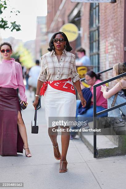 Guest wears shoulder-length black hair styled in soft waves, tortoiseshell oval sunglasses, large gold hoop earrings with layered gold necklaces and...