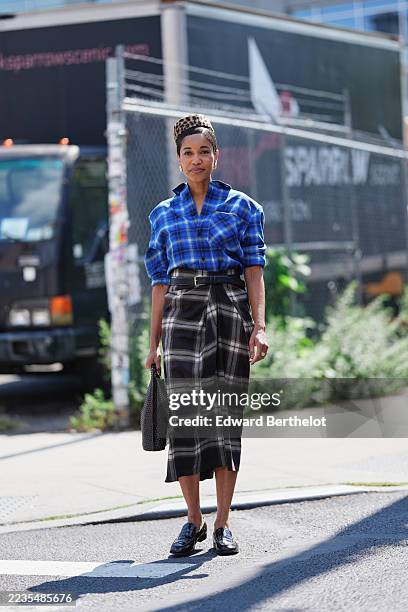 Guest wears short natural hair styled under a leopard-print pillbox hat, small gold hoop earrings, a rectangular woven black leather handbag, a blue...