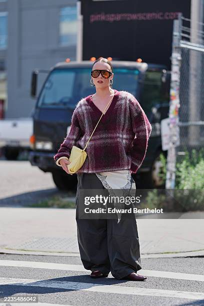 Guest wears slicked-back hair in a low bun, oversized amber-gradient sunglasses with black frames, large gold hoop earrings, a small slouchy yellow...