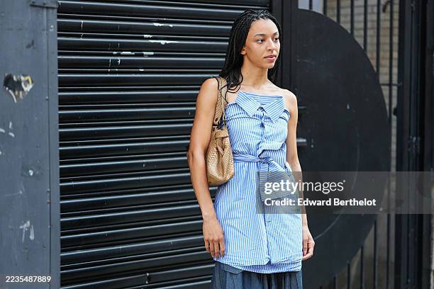 Guest wears long black box braids worn loose over the shoulders, a woven tan leather shoulder bag with slouchy hobo shape and visible metal hardware...