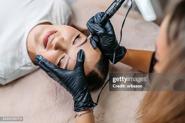 junge frau, die augenbrauen von einer augenbrauentechnikerin in einem schönheitssalon tätowiert lässt - permanent make up stock-fotos und bilder