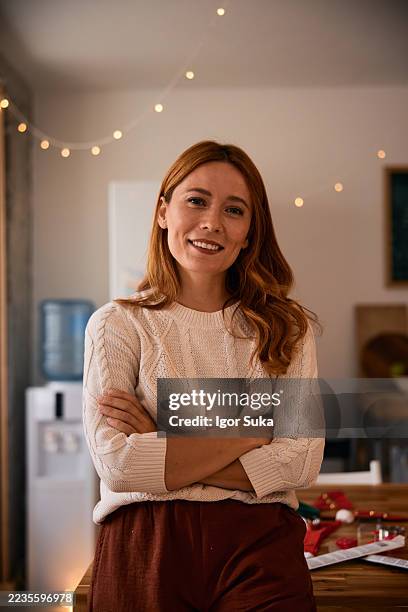 portrait of smiling young woman with crossed arms preparing christmas decorations - festieve stemming stockfoto's en -beelden