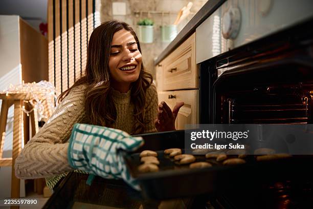 young woman taking a tray of freshly baked christmas cookies out of the oven - ugn bildbanksfoton och bilder