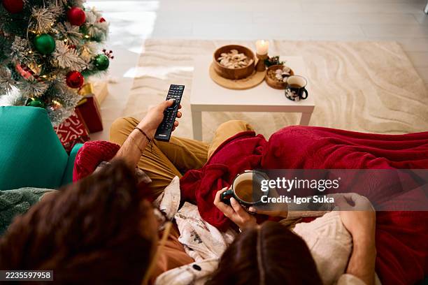 couple relaxing on sofa, watching tv and drinking tea during christmas holidays - hot drink stock pictures, royalty-free photos & images