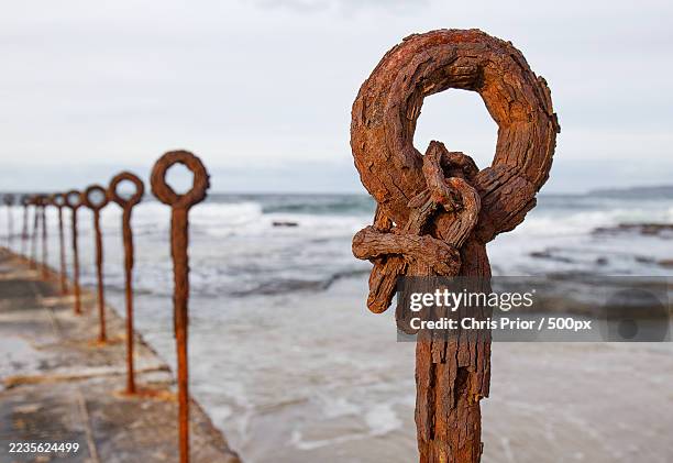 close-up of a rusty metal post with a ring on a beach against a cloudy sky, with waves in the background,newcastle,australia - newcastle nouvelle galles du sud photos et images de collection