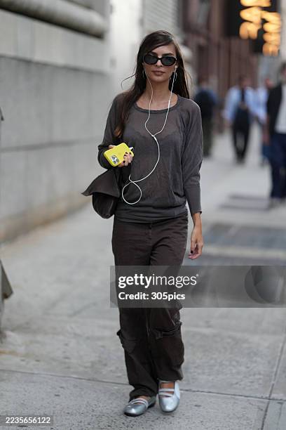 Emily Ratajkowski is seen wearing a loose long-sleeve dark brown top, matching dark brown relaxed-fit pants, silver mary jane style shoes, carrying a...