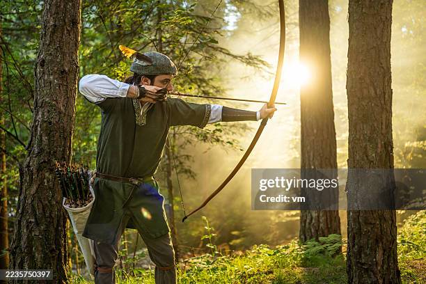 medieval archer drawing bow in sunlit forest - fossil stock pictures, royalty-free photos & images