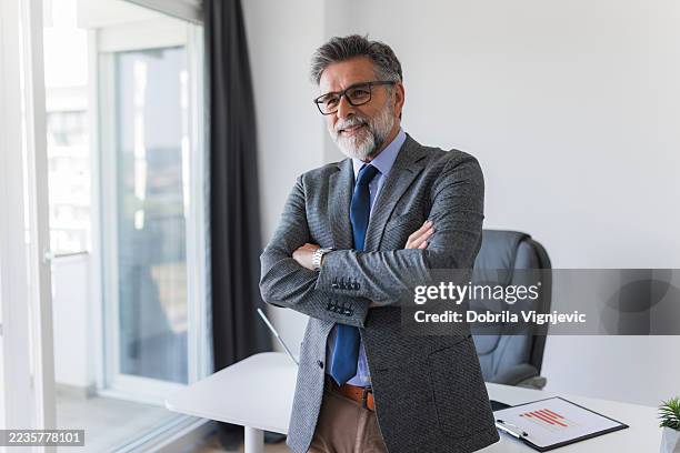 empresario senior seguro de sí mismo sonriendo con los brazos cruzados en la oficina - director financiero fotografías e imágenes de stock