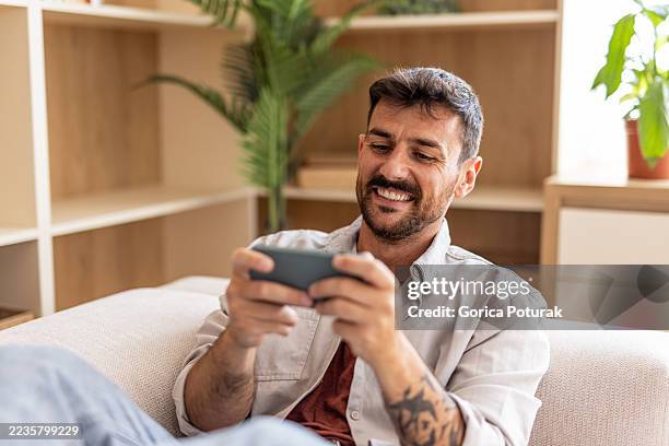 homme heureux jouant à des jeux vidéo sur smartphone à la maison - jeu mobile photos et images de collection