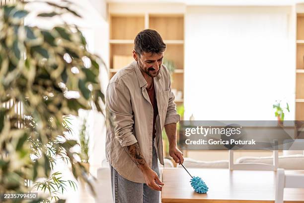 smiling man dusting wooden table in modern apartment - man dusting stock pictures, royalty-free photos & images
