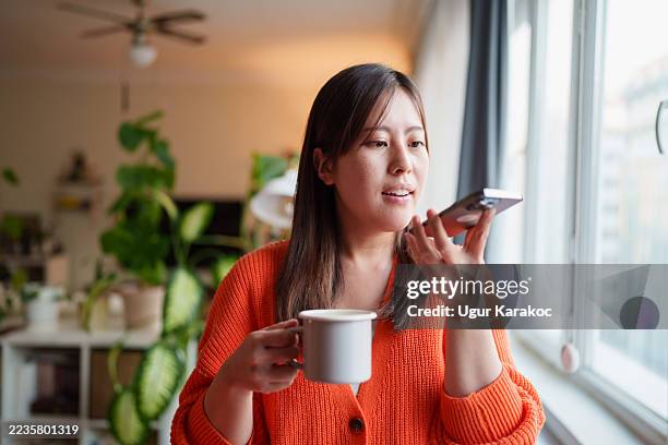 woman using voice assistant on smartphone while holding mug - speech recognition stock pictures, royalty-free photos & images