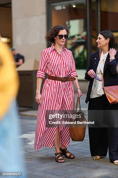 Guest wears short curly dark brown hair, black rectangular sunglasses, a gold chain necklace and a gold bangle with a silver watch, carries a tan...