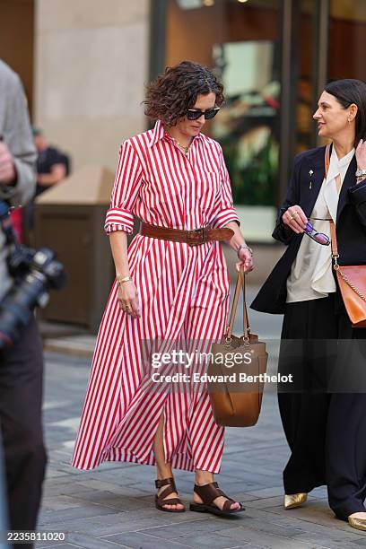 Guest wears short curly dark brown hair, black rectangular sunglasses, a gold chain necklace and a gold bangle with a silver watch, carries a tan...