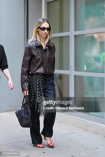 Guest wears shoulder-length straight blonde hair with a center part, black narrow cat-eye sunglasses, multiple silver rings on the left hand, a soft...