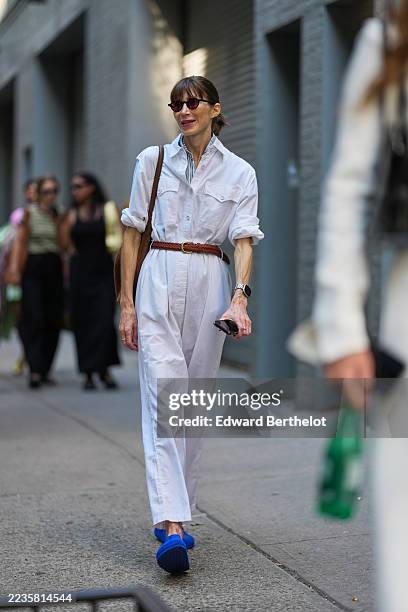 Guest wears their hair pulled back into a low ponytail with straight bangs, small round burgundy sunglasses with dark lenses, a silver metal watch...