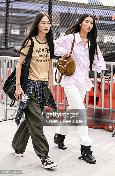Model is seen wearing a Coach t-shirt, gray pants, plaid shirt and black bag with a model wearing a pink button shirt, white pants and black boots...