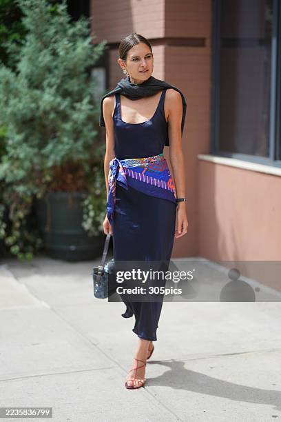 Lydia Zacharis is seen wearing a Haider Ackermann navy satin dress, a Hermes scarf wrapped around the waist, a black sweater wrapped over the...