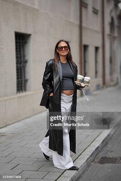 Anna Winter is seen wearing a long buttoned black leather coat with a sleek finish from Anine Bing; a dark grey fitted crop top, revealing a hint of...