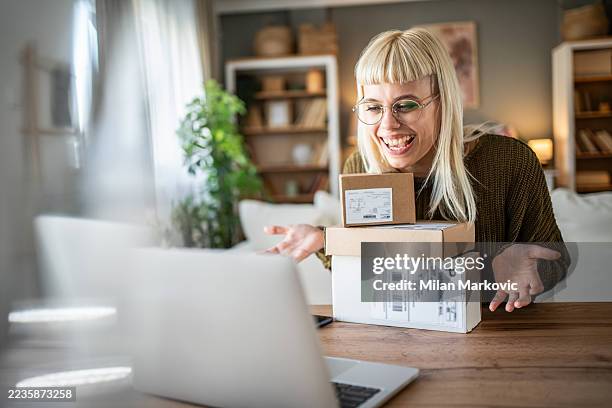 mujer joven mostrando paquetes durante una videollamada en una computadora portátil - espacio de trabajo virtual compartido fotografías e imágenes de stock