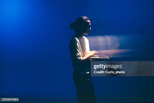 an asian man working in software development, cybersecurity analysis or database code protection works on a laptop under neon blue light. - gegenlicht stock-fotos und bilder