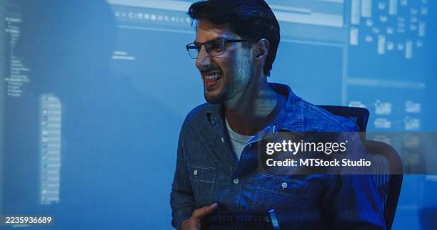 cheerful young hispanic male programmer jokingly strums his computer keyboard like a guitar in a dark office late into the night. software developer, artificial intelligence. - java code stock pictures, royalty-free photos & images