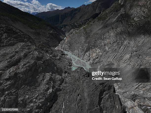 In this aerial view the gravel-covered and blackened Aletsch Glacier arrives at a stream of its meltwater in a gorge the glacier once filled on...