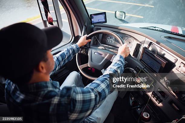 männlicher lkw-fahrer, der einen modernen sattelschlepper auf einer asphaltierten straße fährt - lkw kabine stock-fotos und bilder