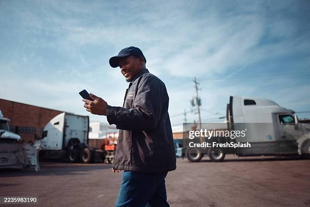 man smiling and using smartphone in outdoor truck yard on a sunny day - vrachtwagenchauffeur stockfoto's en -beelden