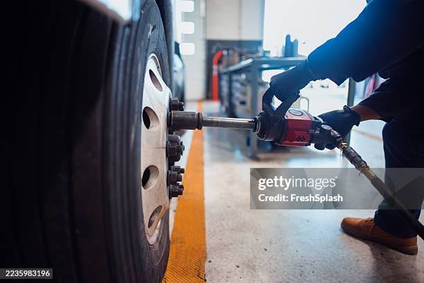mechanic tightening vehicle wheel bolts using a power tool in workshop - vehicle trailer stock pictures, royalty-free photos & images